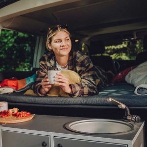 Eine Frau liegt auf einer Matratze in einem Van, vor ihr eine Küche