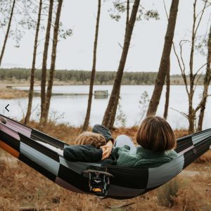 Ein Paar liegt gemütlich in einer karierten Hängematte. Sie befindet sich am See